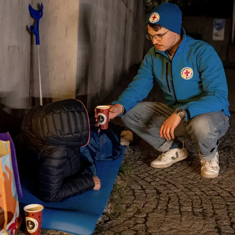 Obdachloser Mensch bekommt einen warmen Tee von einem Mitarbeiter der Bahnhofsmission Würzburg