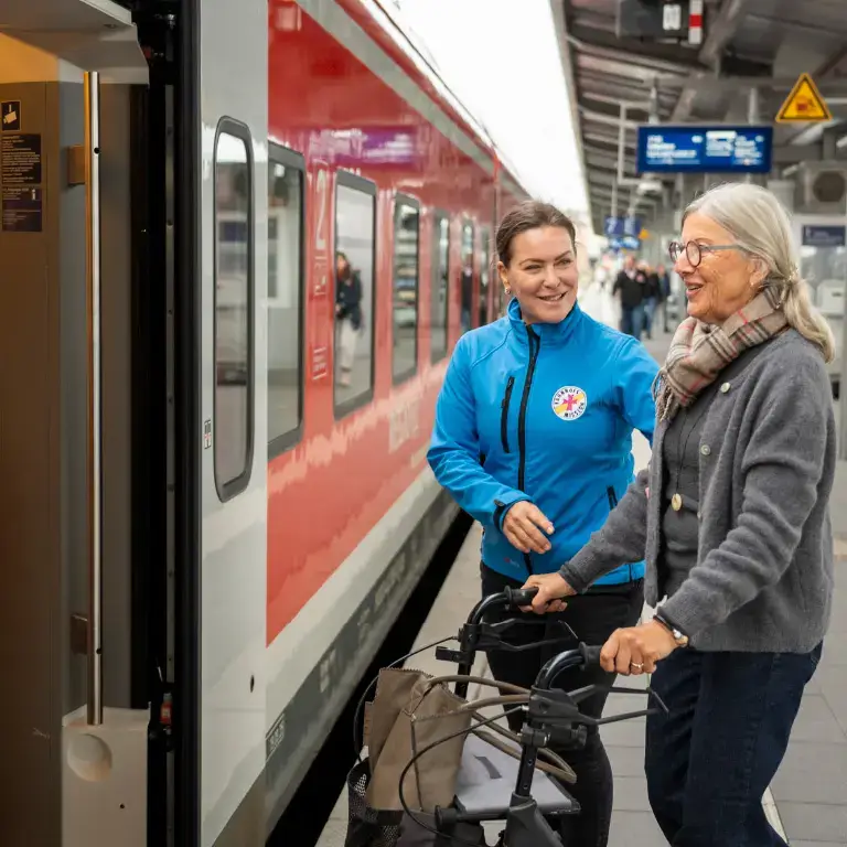 Ehrenamtliche der Bahnhofsmission Würzburg hilft einer älteren Dame mit Rollator am Gleis beim Einstieg in den Zug